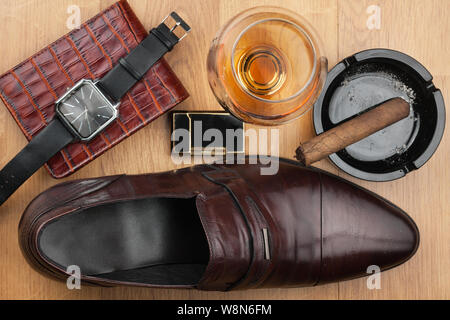 Männer Zubehör. Braun elegante Schuhe, Geldbörse, Alkohol und Zigarren auf hölzernen Tisch. Ansicht von oben. Stockfoto