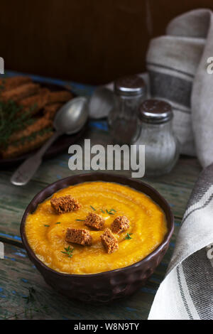 Kürbis- oder Karottencremesuppe mit Croutons und Thymian auf Holzgrund. Rustikaler Stil. Stockfoto