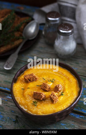 Kürbis- oder Karottencremesuppe mit Croutons und Thymian auf Holzgrund. Rustikaler Stil. Stockfoto