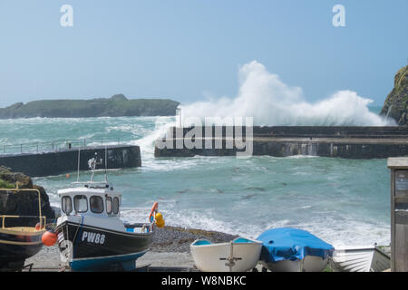 Mullion Cove, Cornwall, UK. 10 Aug, 2019. Starke Winde und eine Flut kraft Wellen über den Wellenbrecher in Mullion Cove im Süden von Cornwall. Obwohl warme und sonnige Niemand auf der Mauer heute sitzt. Credit: Herr Standfast/Alamy leben Nachrichten Stockfoto