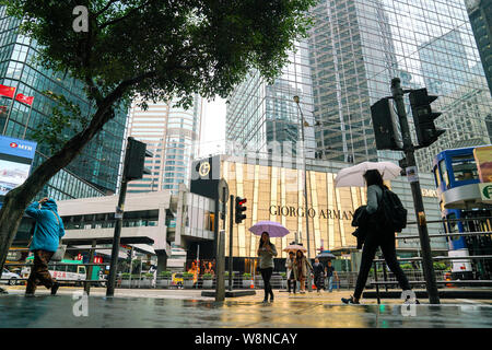 Central, Hong Kong - 14. März 2019: Menschen zu Fuß auf der Straße während der regnerischen Tag mit Giorgio Armani Outlet im Hintergrund Stockfoto