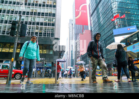 Central, Hong Kong - 14. März 2019: Massen von Menschen zu Fuß und über die Straße an einem regnerischen Tag. Stockfoto
