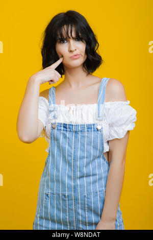 Junge Dame in stilvollem Outfit stossen Wange niedlich und Kamera beim Stehen auf gelbem Hintergrund Stockfoto