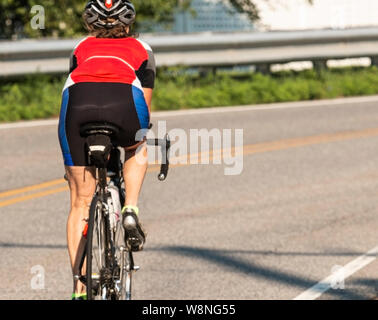 Eine weibliche Radfahrer reiten auf eine leere Straße Ausbildung für einen Triathlon von der Kamera entfernt mit offenen Zeitraum vor ihr. Stockfoto