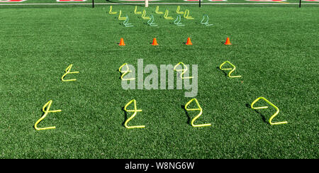 Zeilen werden für Geschwindigkeit und Agilität der Praxis auf einem grünen Rasenfeld mit gelben Banane Hürden und kleine orange Kegel eingestellt. Stockfoto
