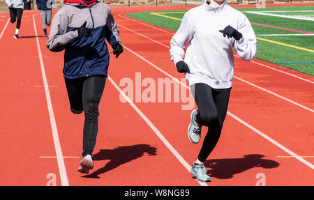 High School Mädchen, die Zwei und zwei in Bahnen auf einem sonnigen, aber kalten Nachmittag Training für Leichtathletik. Stockfoto