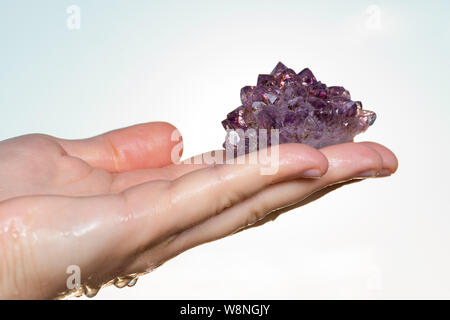 Amethyst Rosette oder Cluster Ende, mit Goethit Einschlüsse aus Brasilien in die Hand der Frau bei Sonnenaufgang vor dem See. Stockfoto