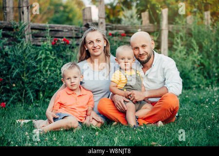 Schöne happy Kaukasischen Ukrainische Familie von vier Personen im Park im Sommer Tag. Vater und Mutter, ihre zwei Söhne Brüder Geschwister umarmen. Lebensstil Stockfoto