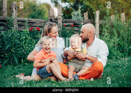 Schöne happy Kaukasischen Ukrainische Familie von vier Personen im Park im Sommer Tag. Vater und Mutter, ihre zwei Söhne Brüder Geschwister umarmen. Lebensstil Stockfoto