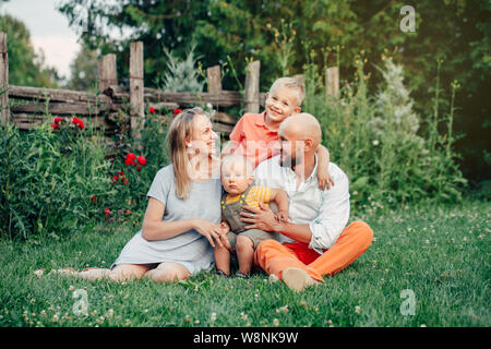 Schöne happy Kaukasischen Ukrainische Familie von vier Personen im Park im Sommer Tag. Vater und Mutter, ihre zwei Söhne Brüder Geschwister umarmen. Lebensstil Stockfoto