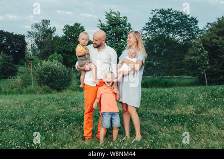 Schöne happy Kaukasischen Ukrainische Familie von vier Personen im Park im Sommer Tag. Vater und Mutter, ihre zwei Söhne Brüder Geschwister umarmen. Lebensstil Stockfoto