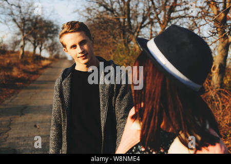 Nicht erkennbare Weiblichen im stylischen Hut zurück drehen und auf der Suche nach gutaussehenden jungen Mann, während im Herbst Landschaft zusammen gehen. Anonyme Frau looki Stockfoto