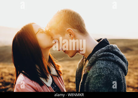 Seitenansicht des netten jungen weiblichen Küssen hübscher Kerl in der Stirn, während im Feld zusammen. Frau küssen Freund in der Stirn in der Natur Stockfoto