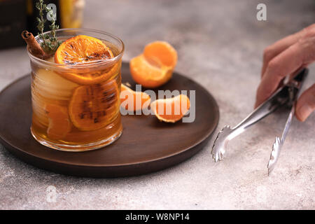 Whiskey Sour Cocktail mit Tangerine Schichten und Eiswürfel mit Zimt und Thymian eingerichtet. Alkohol trinken Hintergrund. Stockfoto