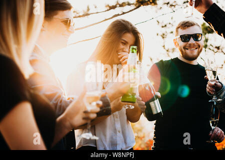 Junge Männer und Frauen lachen und Trinken feinen Alkohol, während die Zeit in der Natur an einem sonnigen Tag Stockfoto