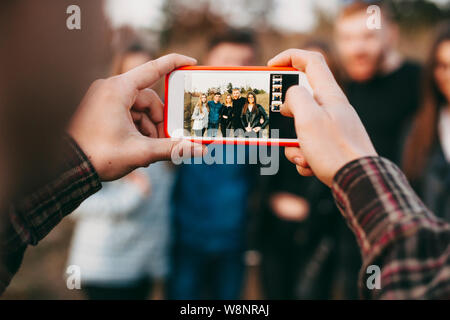 Hände von anonymen mit männlichen Smartphone Foto der Gruppe junger Freunde, in der Natur zu nehmen. Erntegut Hände sie Bilder von Freunden Stockfoto