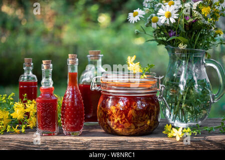 Flaschen mit roter Öl aus Johanniskraut Blüten, in einem Garten fotografiert gemacht Stockfoto