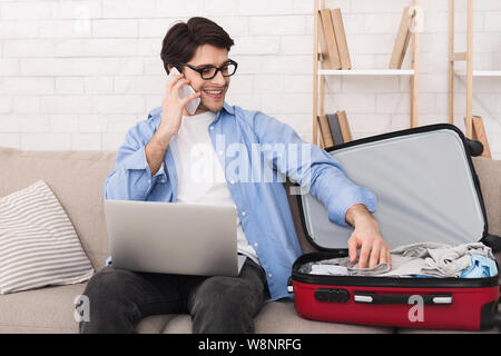 Junger Mann Vorbereitung für Reise und am Telefon sprechen Stockfoto