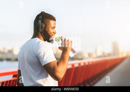 Junge schwarze Mann Trinkwasser auf der Brücke Stockfoto