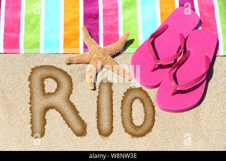 Rio Strand Konzept. Ansicht von oben ot das Wort RIO auf goldenen Sand mit einem Seestern, pink Flip Flops und Handtuch konzeptionelle eines Sommer Urlaub und Reisen in Rio de Janiero, Brasilien geschrieben Stockfoto