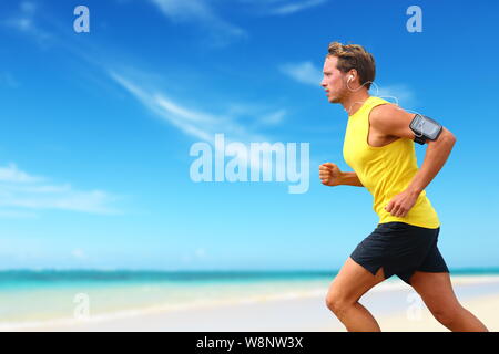 Läufer laufen hören Smartphone Musik am Strand cardio Workout. Männliche Athlet joggen am Ocean Beach oder am Wasser, Arbeiten mit Smart Phone App gerät und Ohrhörer im Sommer. Stockfoto