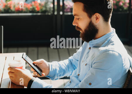 Seitenansicht der junge Bartgeier über Handy männlichen und Holding Schale am Tisch im Freien sitzen Stockfoto