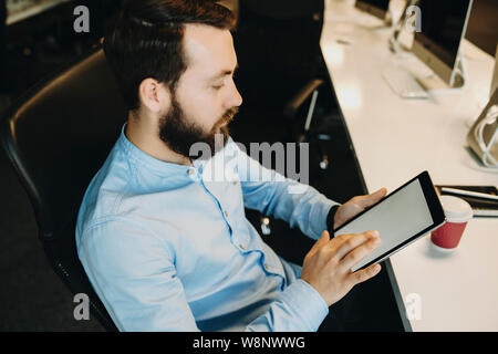Seitenansicht von nachdenklich erwachsener Mann sitzt mit digitalen Tablet und Arbeiten Stockfoto