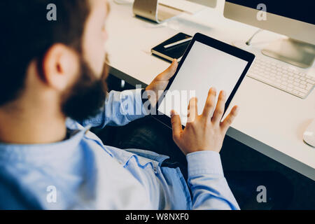 Erntegut bärtigen Kerl berühren leerer Bildschirm von modernen Tablet während am Schreibtisch im modernen Büro zu sitzen. Anonyme Büroangestellter mit Tablet Stockfoto