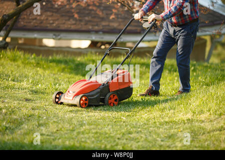 Mähen Trimmer - Arbeiter Schneiden von Gras im grünen Hof bei Sonnenuntergang. Mann mit elektrischer Rasenmäher, Rasen mähen. Gärtner schneiden Garten. Stockfoto