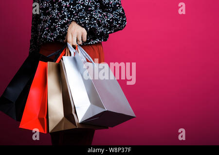 Erntegut Blick auf schlanke Frau im gemusterten Shirt holding Papier Einkaufstüten in der Hand auf rosa Hintergrund Stockfoto