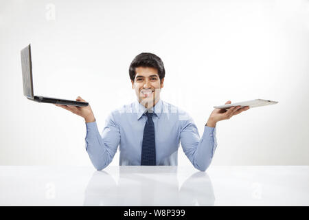 Ein Geschäftsmann, der ein Notebook mit einem digitalen Tablet vergleicht Stockfoto