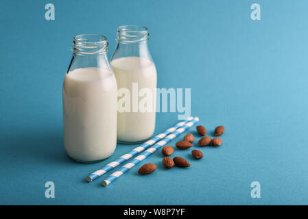 Mandelmilch in Flaschen mit Mandeln und Trinkhalme auf blauem Hintergrund Stockfoto
