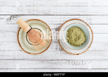 Matcha Grüntee in Pulver- und bambusbesen auf weißem Holz- Hintergrund. Ansicht von oben. Stockfoto