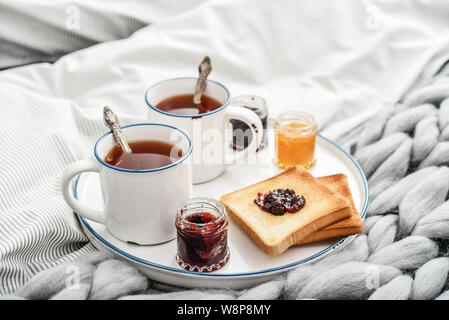 Fach mit zwei Tassen schwarzen Tee, verschiedene Marmelade in Gläser und Toast zum Frühstück am Bett closeup Stockfoto