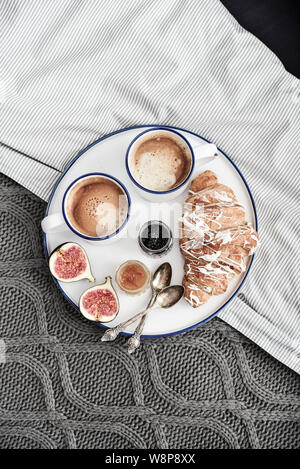 Fach mit zwei Tassen Kaffee, verschiedene Marmelade in Gläser und Croissant zum Frühstück am Bett, Ansicht von oben Stockfoto