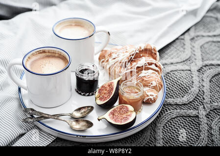 Fach mit zwei Tassen Kaffee, verschiedene Marmelade in Gläser und Croissant zum Frühstück am Bett Stockfoto