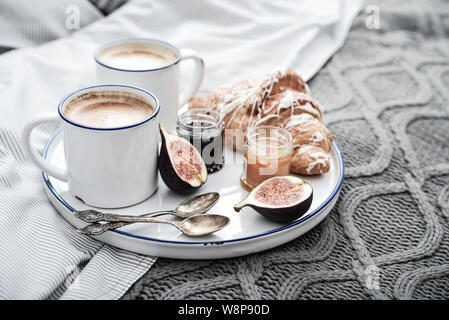 Fach mit zwei Tassen Kaffee, verschiedene Marmelade in Gläser und Croissant zum Frühstück am Bett Stockfoto