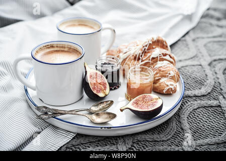 Fach mit zwei Tassen Kaffee, verschiedene Marmelade in Gläser und Croissant zum Frühstück am Bett Stockfoto