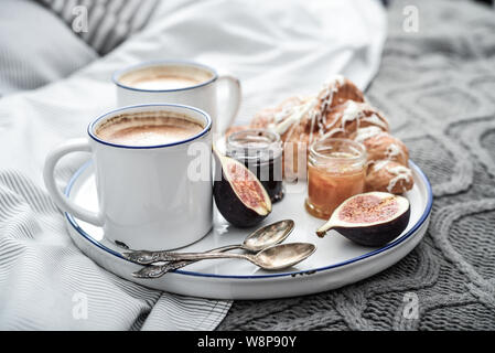 Fach mit zwei Tassen Kaffee, verschiedene Marmelade in Gläser und Croissant zum Frühstück am Bett Stockfoto