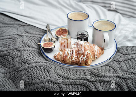 Fach mit zwei Tassen Kaffee, verschiedene Marmelade in Gläser und Croissant zum Frühstück am Bett Stockfoto