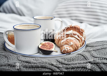 Fach mit zwei Tassen Kaffee, verschiedene Marmelade in Gläser und Croissant zum Frühstück am Bett Stockfoto