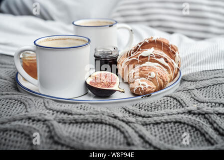 Fach mit zwei Tassen Kaffee, verschiedene Marmelade in Gläser und Croissant zum Frühstück am Bett Stockfoto