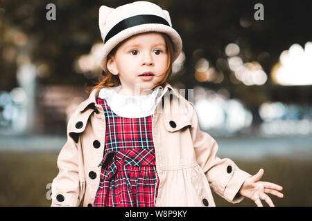 Herbst Portrait von Baby Mädchen 2-3 Jahre alten tragen stilvolle Trenchcoat und Hut draußen im Park. Stockfoto