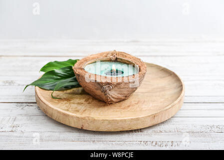 Kerze in Coconut Shell auf roun Holz- Fach auf hellen Hintergrund. Spa-Konzept. Stockfoto