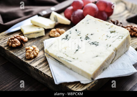 Scheibe Gorgonzola Käse auf Schneidebrett serviert closeup mit Trauben und Nüssen Stockfoto