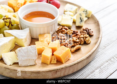 Käseplatte - verschiedene Arten von Käse mit Honig, Nüsse und Trauben auf einem weißen Holz- Hintergrund closeup Stockfoto