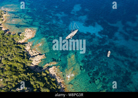 Einen atemberaubenden Blick auf ein luxuriöses Segelboot schwimmt auf einer wunderschönen türkisfarbenen Meer, taucht die Grünen und felsigen Küsten von Sardinien, Italien. Stockfoto