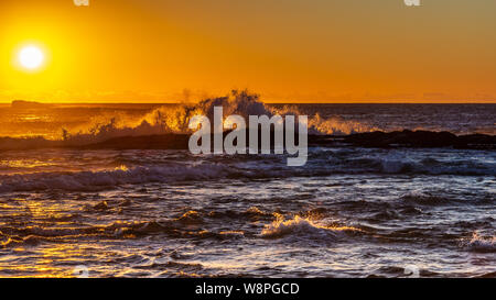 Sonnenaufgang über dem Meer mit Wellen, die auf Felsen Stockfoto