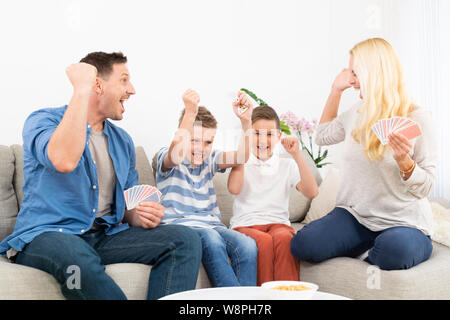 Happy Family spielen Kartenspiel auf Sofa im Wohnzimmer zu Hause und Spaß feiern gemeinsam das Spiel Gewinner Stockfoto