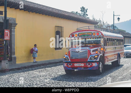 Eine dekorative Chicken Bus auf einer Straße mit Kopfsteinpflaster und ein altes gelbes Gebäude, in Antigua, Guatemala Stockfoto